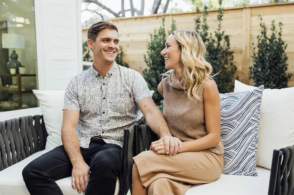 Katie E and Husband sitting on patio furniture at their new TJH-built home, smiling and holding hands.