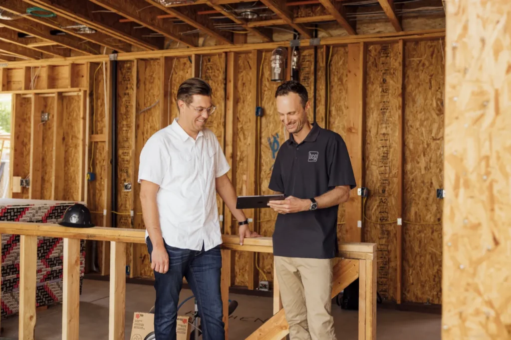 Two construction professionals reviewing plans on a tablet inside a home under construction.