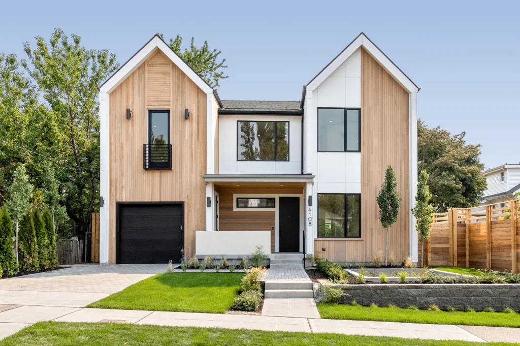 Modern two-story home with wood siding and white exterior panels, featuring a front entry, garage, and landscaped yard.