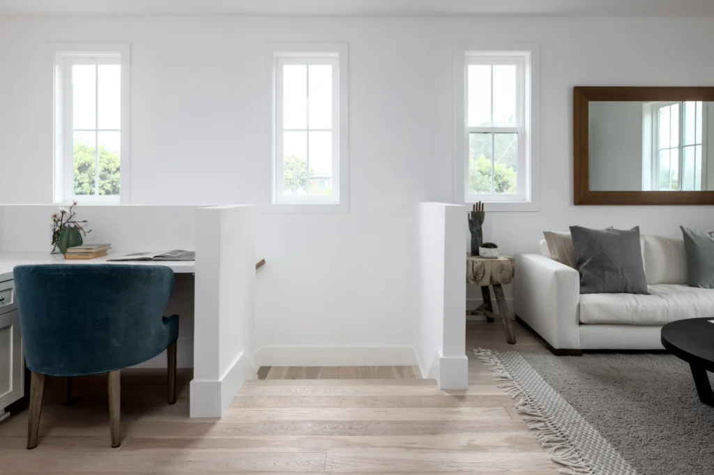 Bright, modern living space with a small desk nook, white walls, light wood flooring, and a cozy seating area with a sofa and rug.