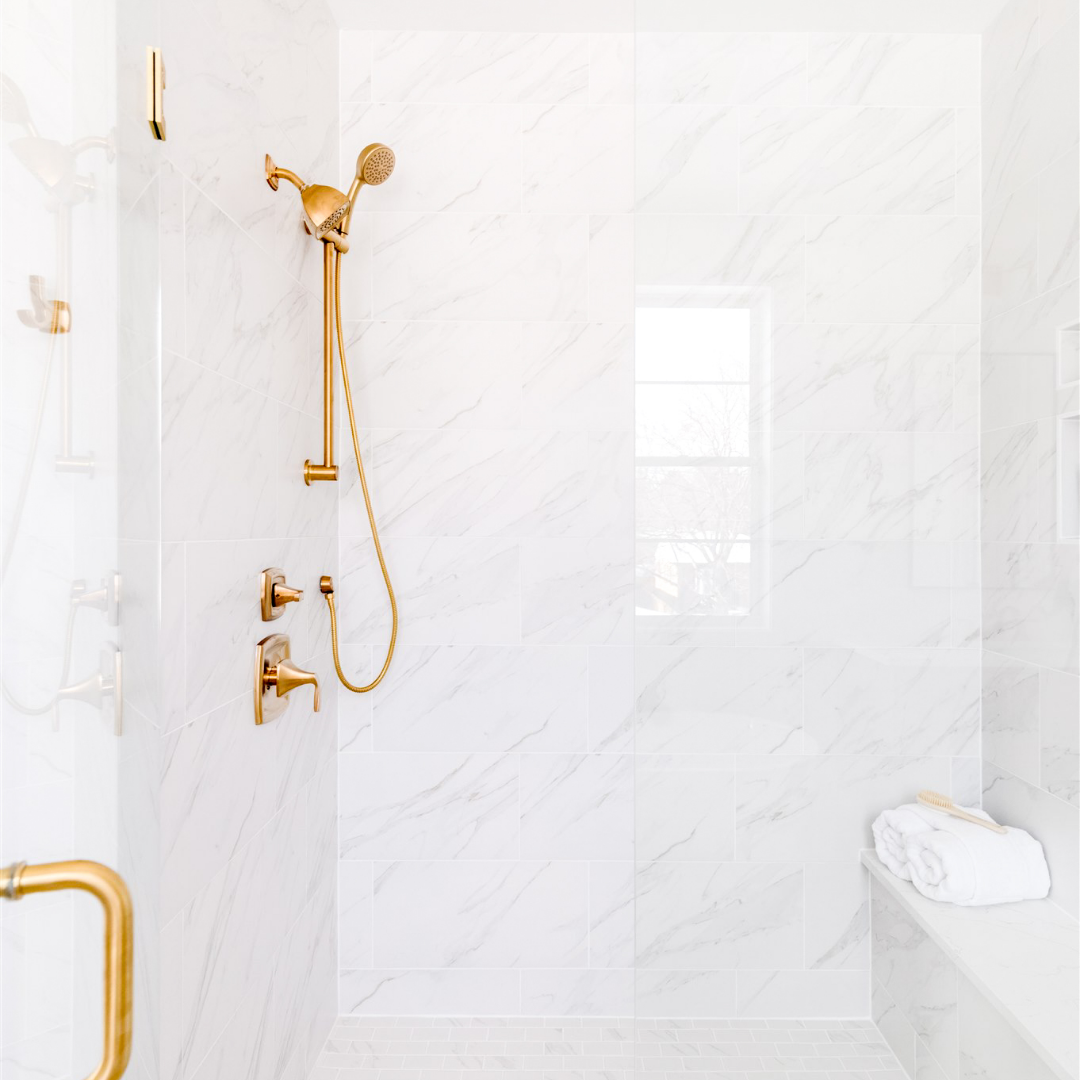 Walk-in shower with brass fixtures and white and gray marble tile.