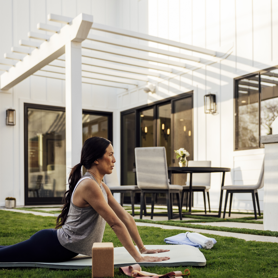Woman doing yoga in backyard with trellised white patio in the backyard