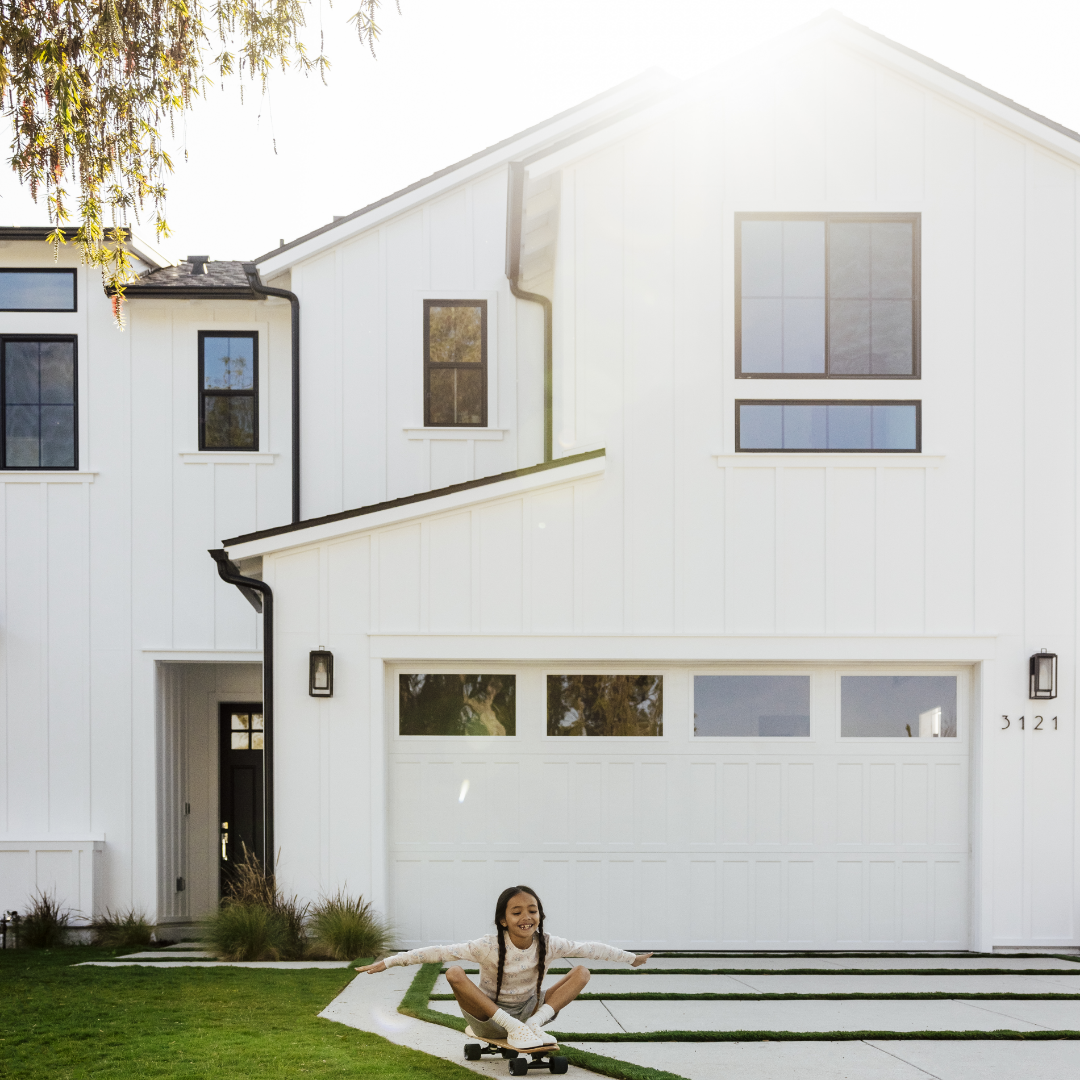 little girl skateboards in front of white modern farmhouse-style home