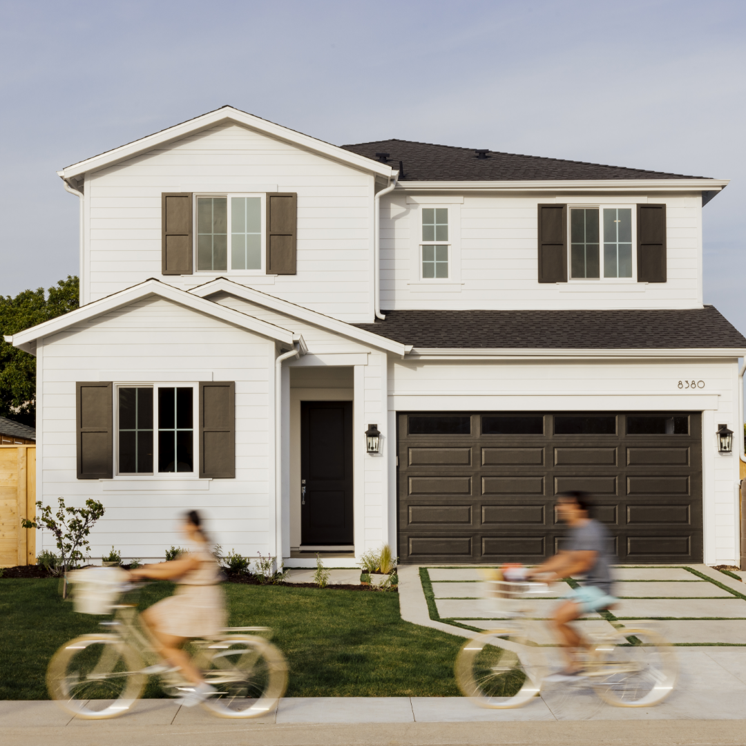 Young man and woman ride bikes past the exterior of a traditional style home built by Thomas James Homes