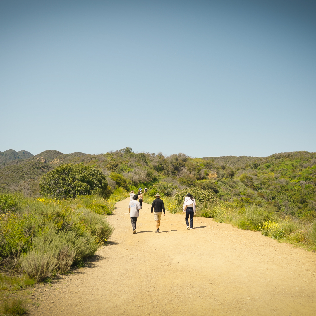 Three people walking on a dirt path hiking in Southern California on a clear day with blue skies