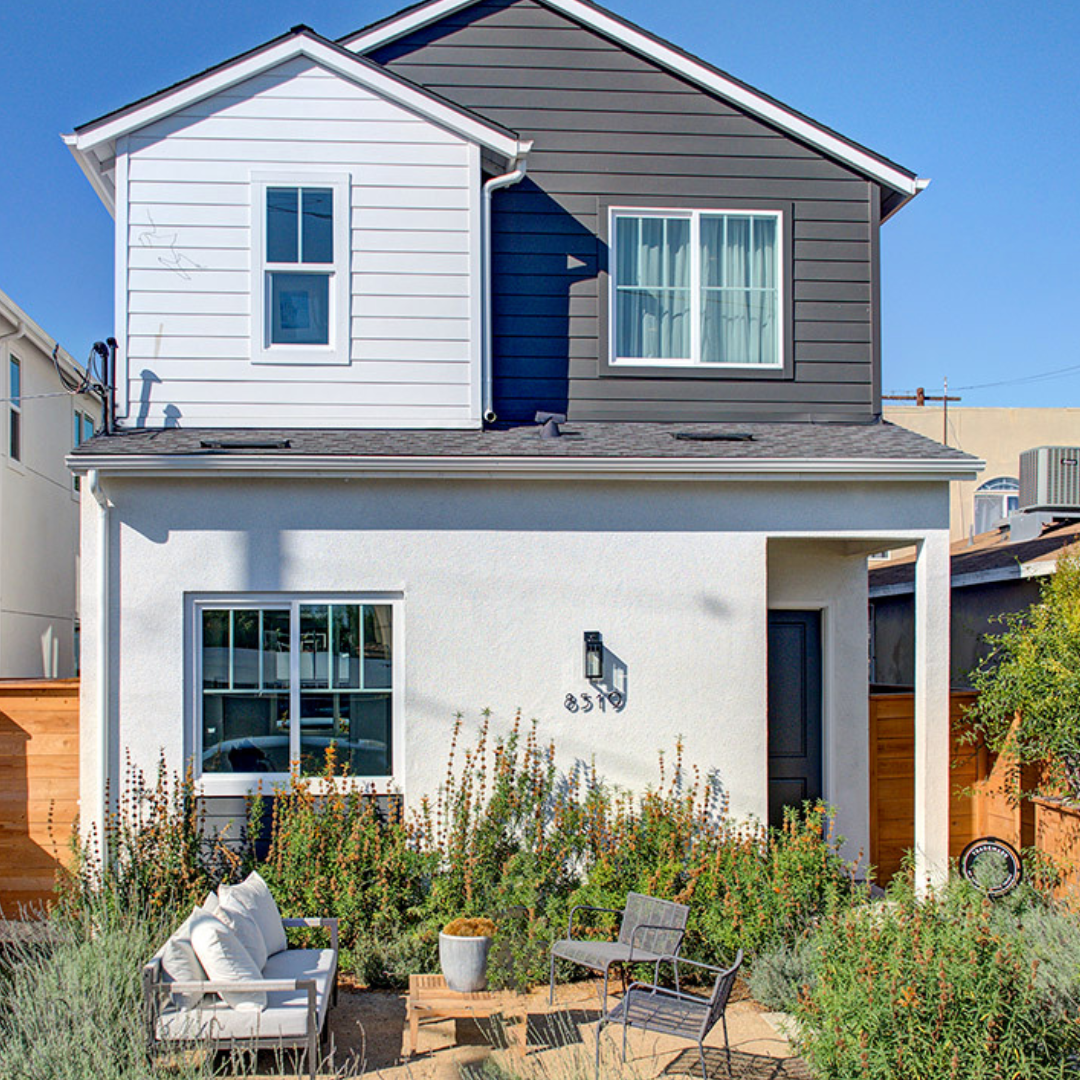 Exterior white and grey house with front garden and green bushes with an outdoor sofa and two chairs for sitting