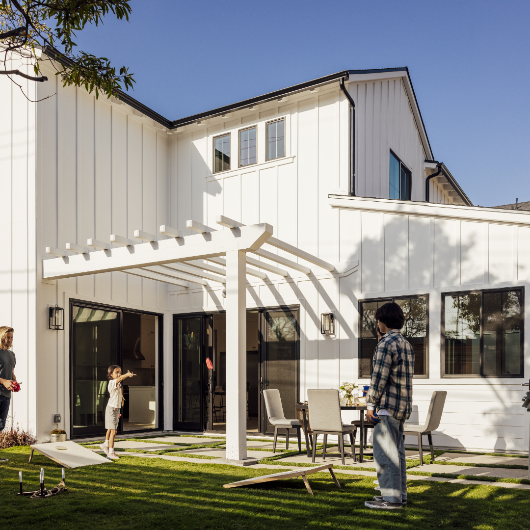 Image of backyard of TJH farmhouse-style home with family playing cornhole