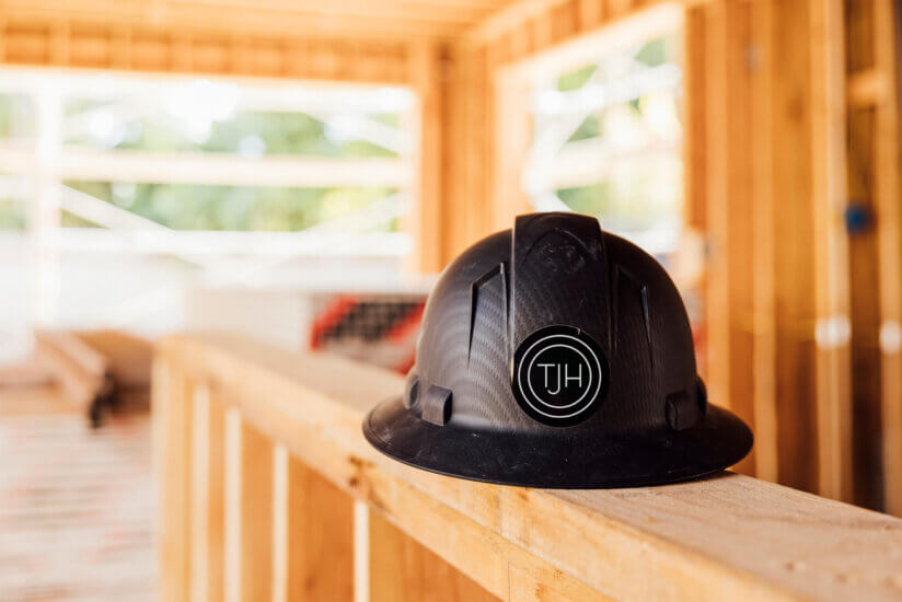 Black hard hat with TJH logo resting on a wood frame inside a home under construction.