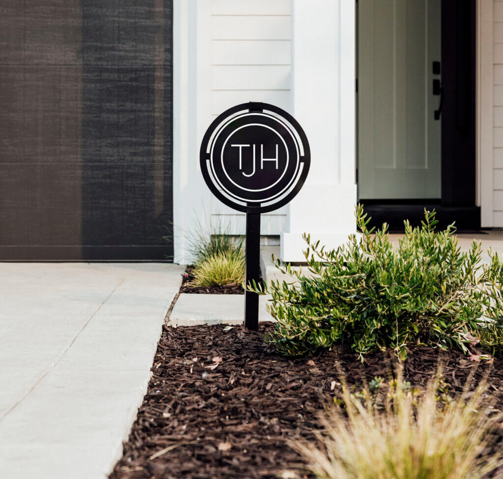 Front exterior of a modern white home, featuring a TJH-branded sign in the landscaped entry.
