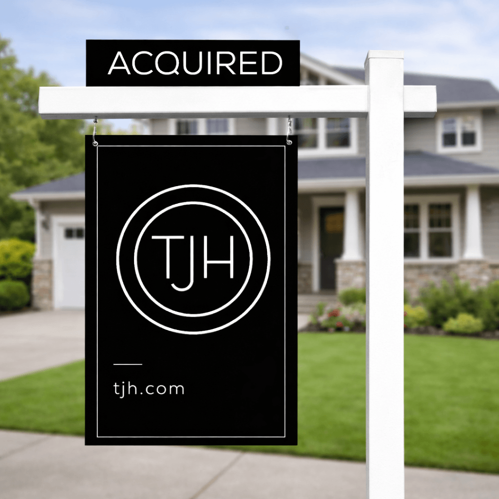TJH “Acquired” real estate sign in front of a blurred suburban Seattle-style home with manicured lawn and neutral exterior.