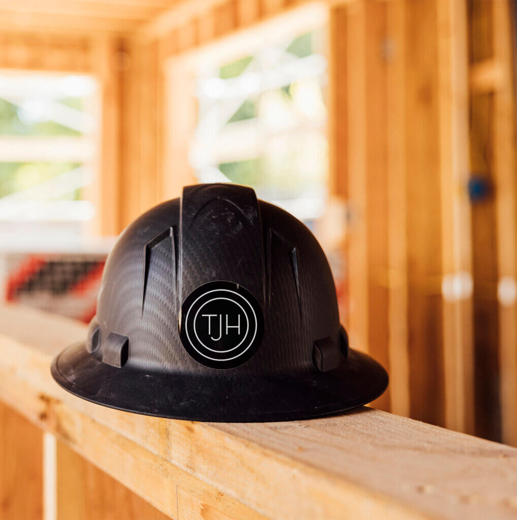 Black hard hat with TJH logo resting on a wood frame inside a home under construction.