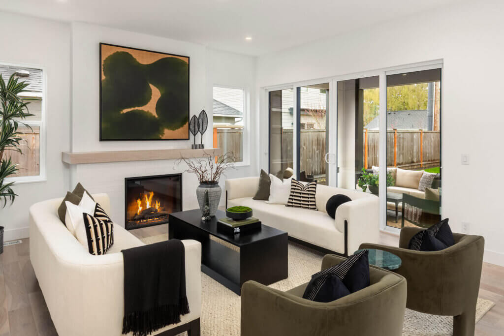 Modern living room with a fireplace, white sofas, green accent chairs, and sliding glass doors opening to a backyard.