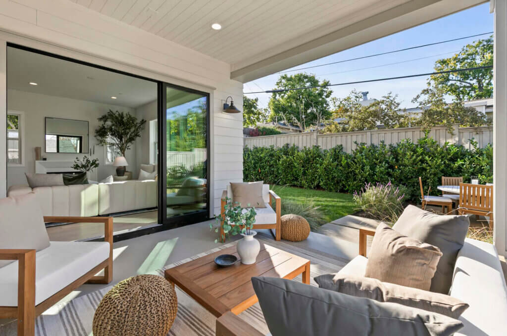 TJH Hollyleaf covered patio with cushioned chairs, wood coffee table, and decorative plants overlooking the backyard