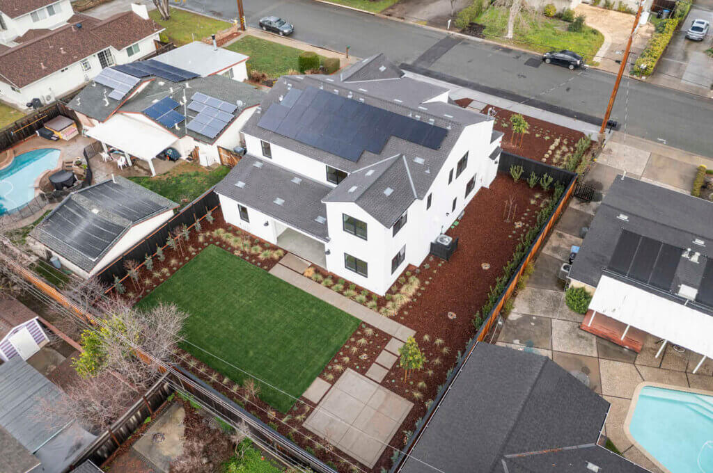Aerial view of TJH Verbena with solar panels, fenced yard, green lawn, and mulch beds