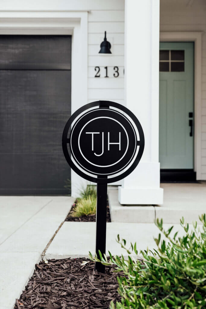 TJH yard sign in front of a newly completed modern home with white exterior, pale green front door, and black garage accents.