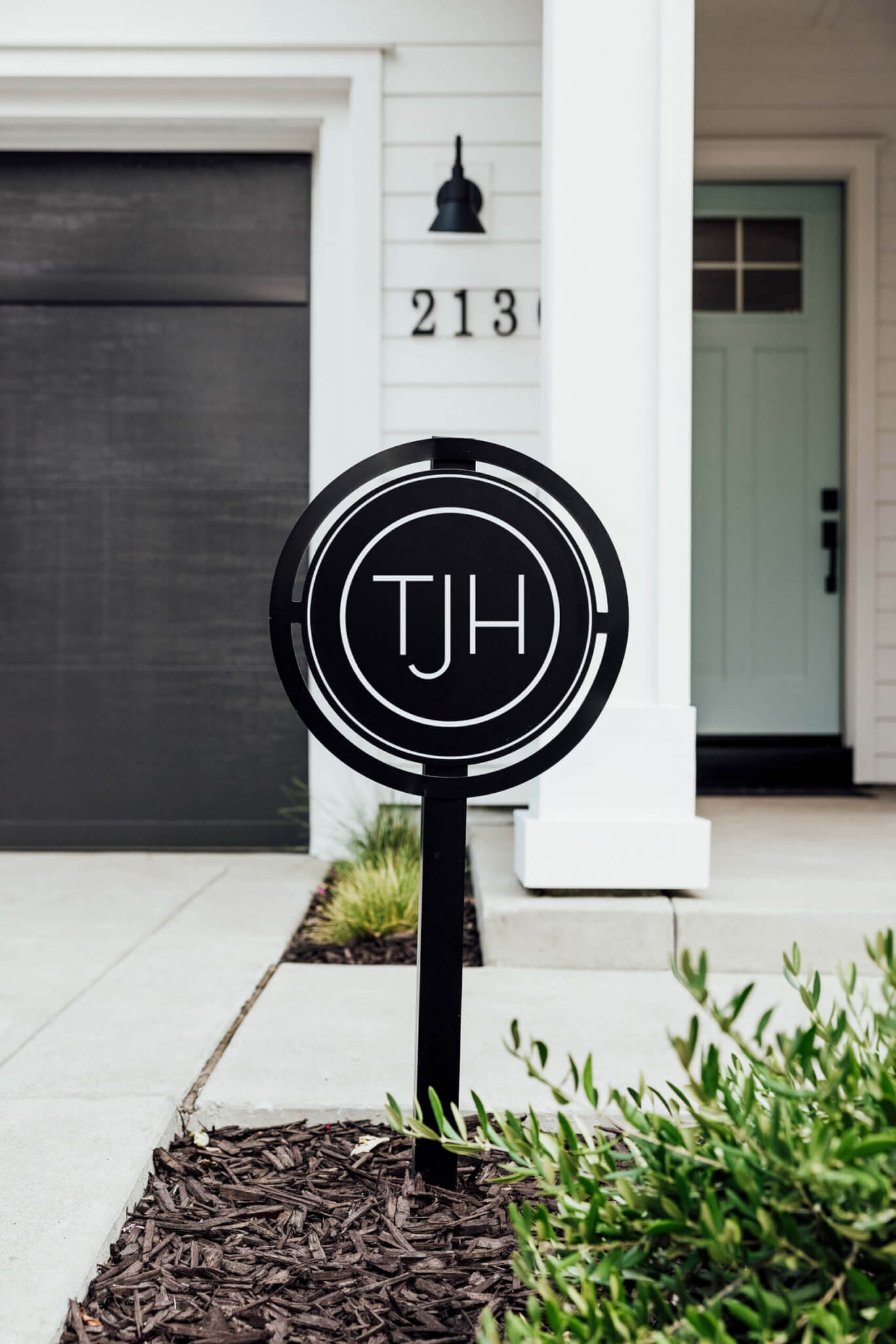 TJH yard sign in front of a newly completed modern home with white exterior, pale green front door, and black garage accents.